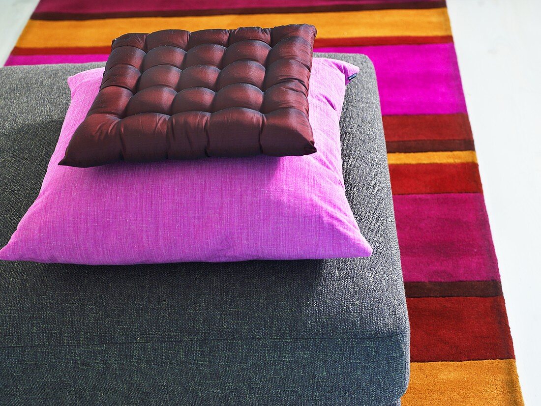 Pillows in assorted shades of red on a gray pad and striped carpet