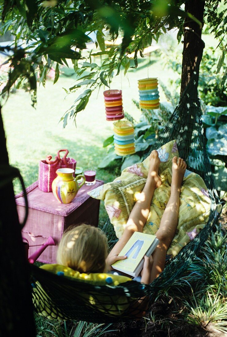 A girl lying in a hammock beneath a tree hung with lanterns