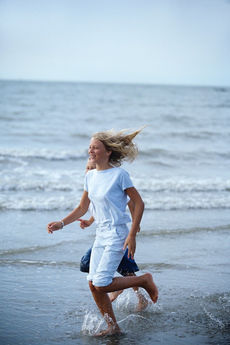 A girl and a boy running along a beach