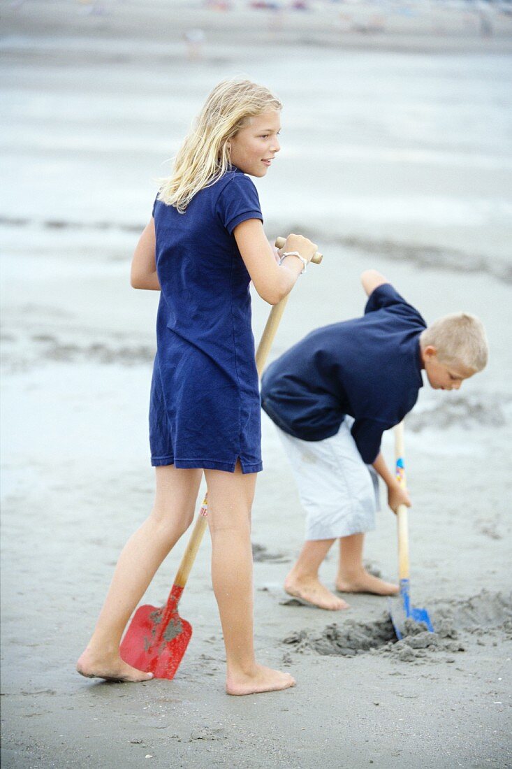 Mädchen und Junge schaufeln Sand am Meer