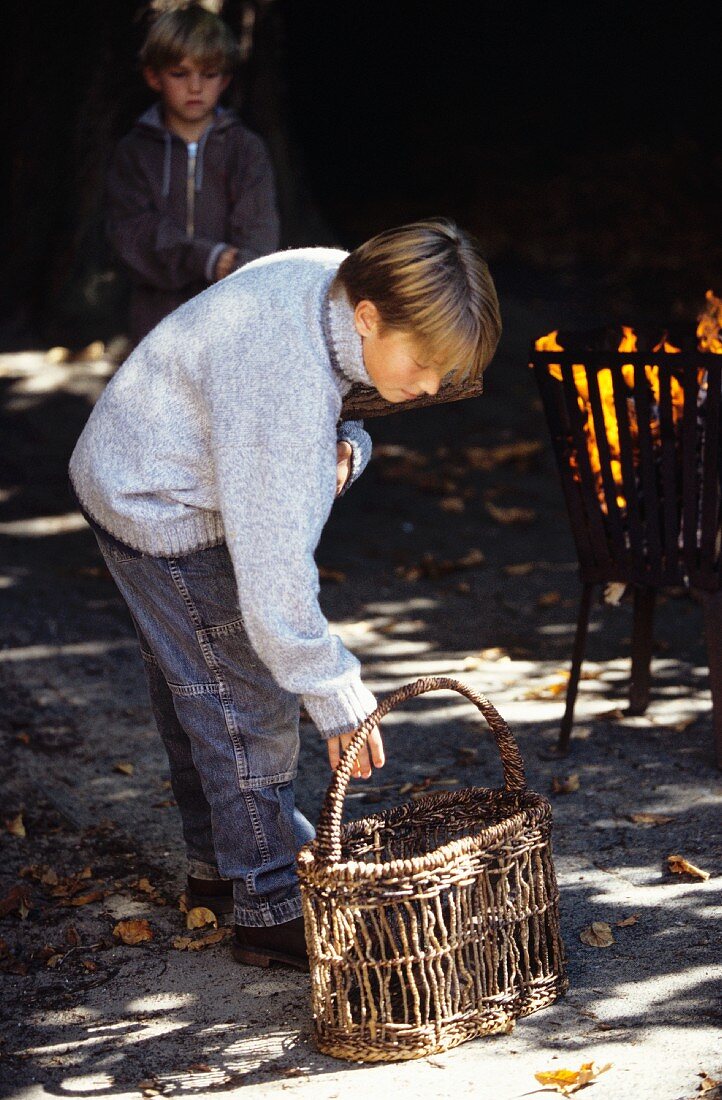 Junge steht neben einem Korb am Feuer