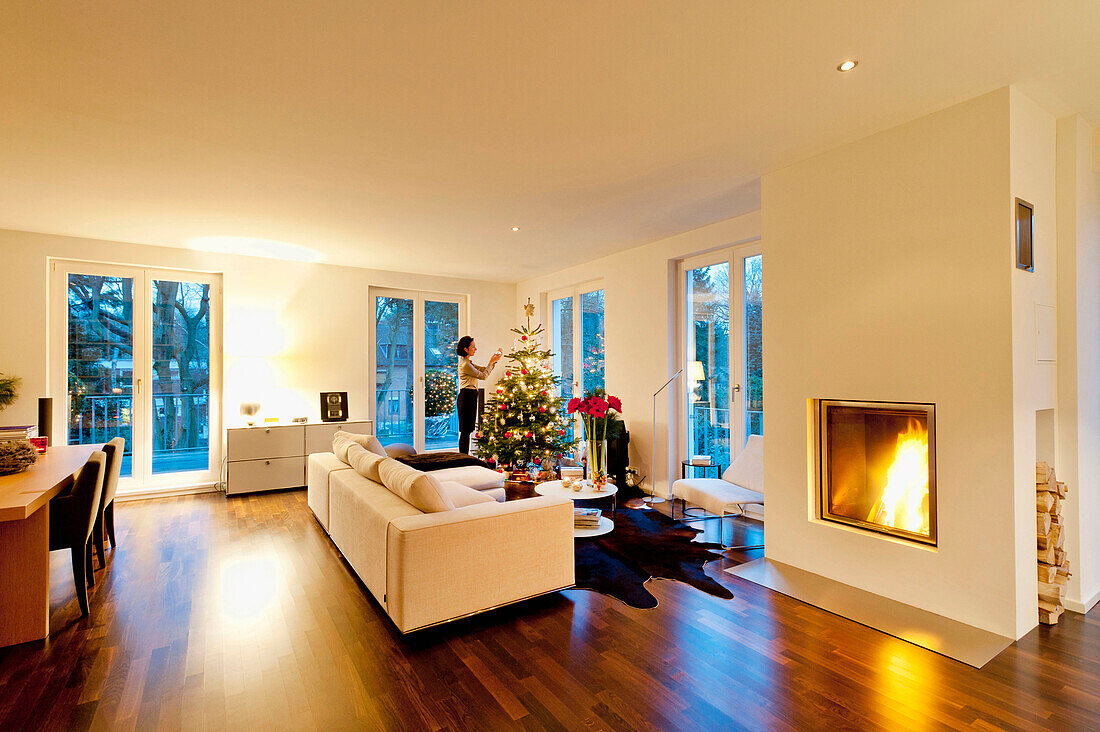 Modern flat with christmas tree and fireplace, woman dressing the tree, Hamburg, Germany