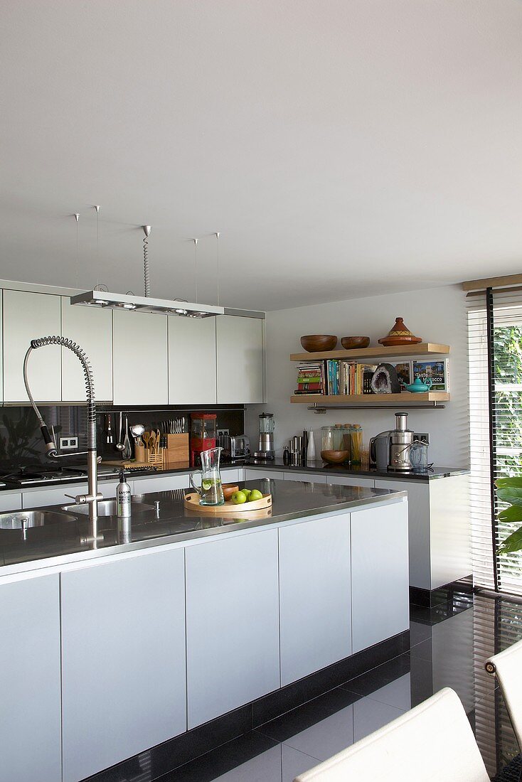 A white fitted kitchen with a free-standing designer kitchen unit and shiny black floor tiles
