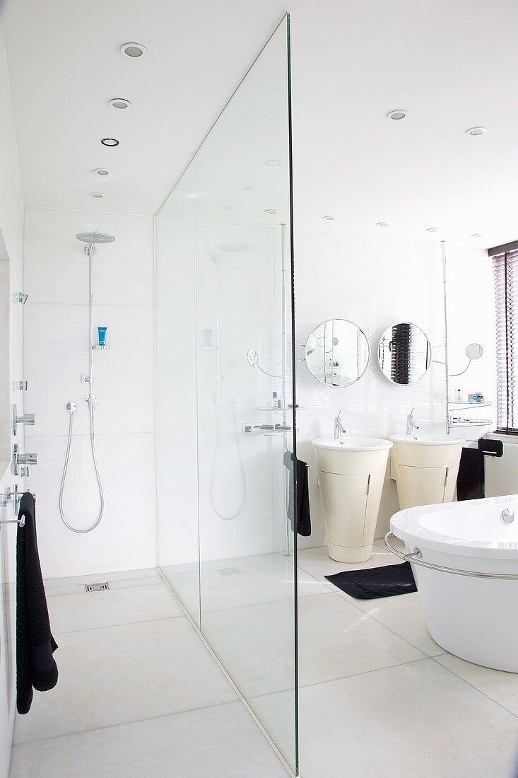 A white bathroom with a shower area separated by a glass wall and contrasting black towels