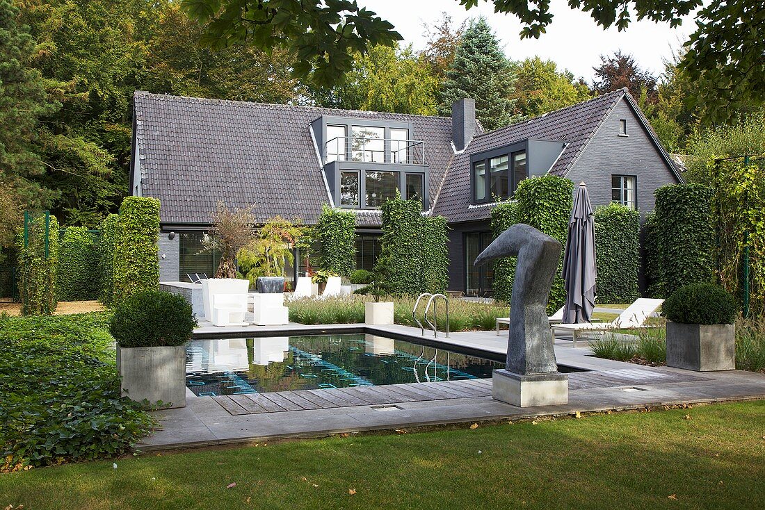 Haus mit grauem Fassadenanstrich, geschnittene Hecken im Garten mit Pool