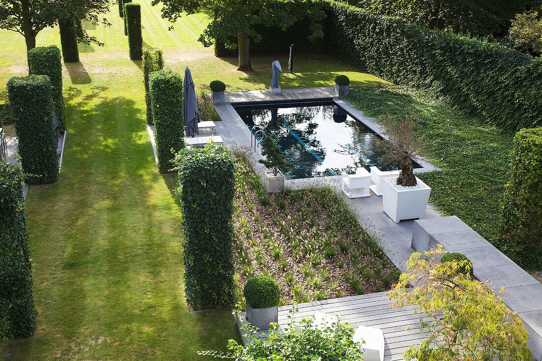 A landscaped, English-style garden with a pool, trimmed hedges and plant boxes