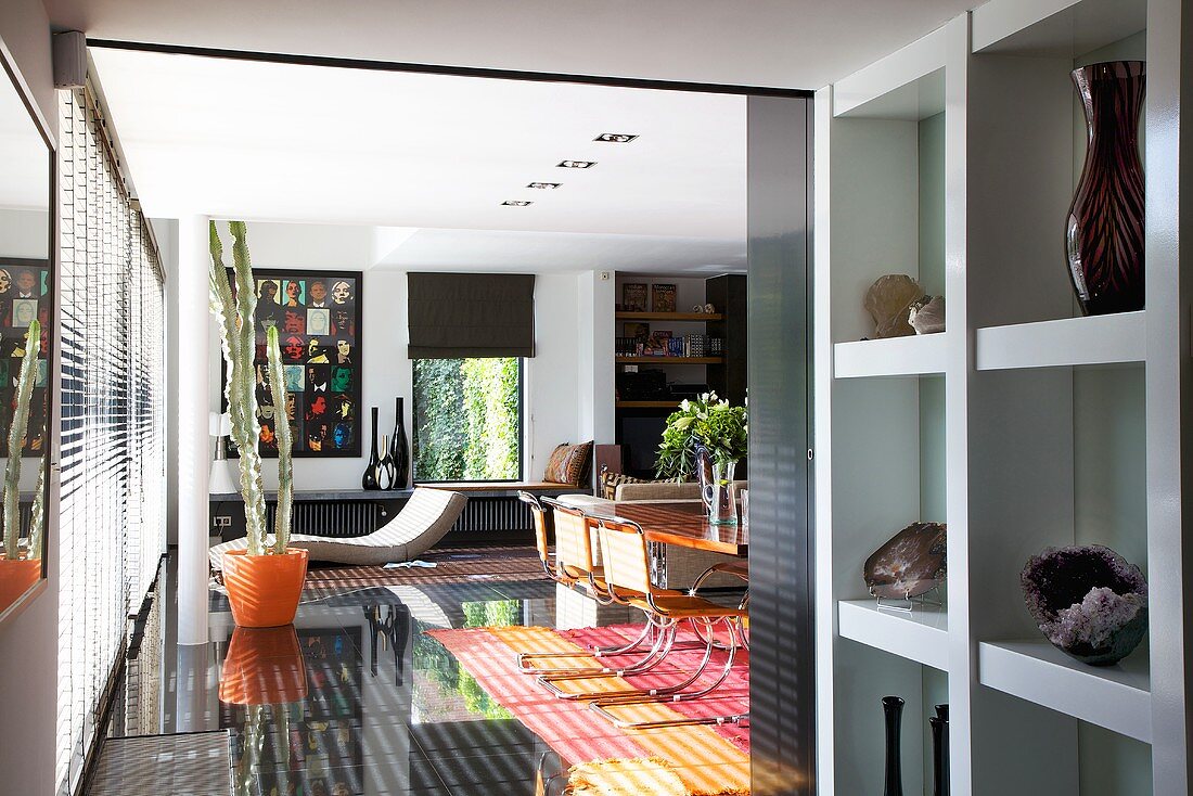 A designer living room with a lounger, an orange plant pot and shiny black floor tiles