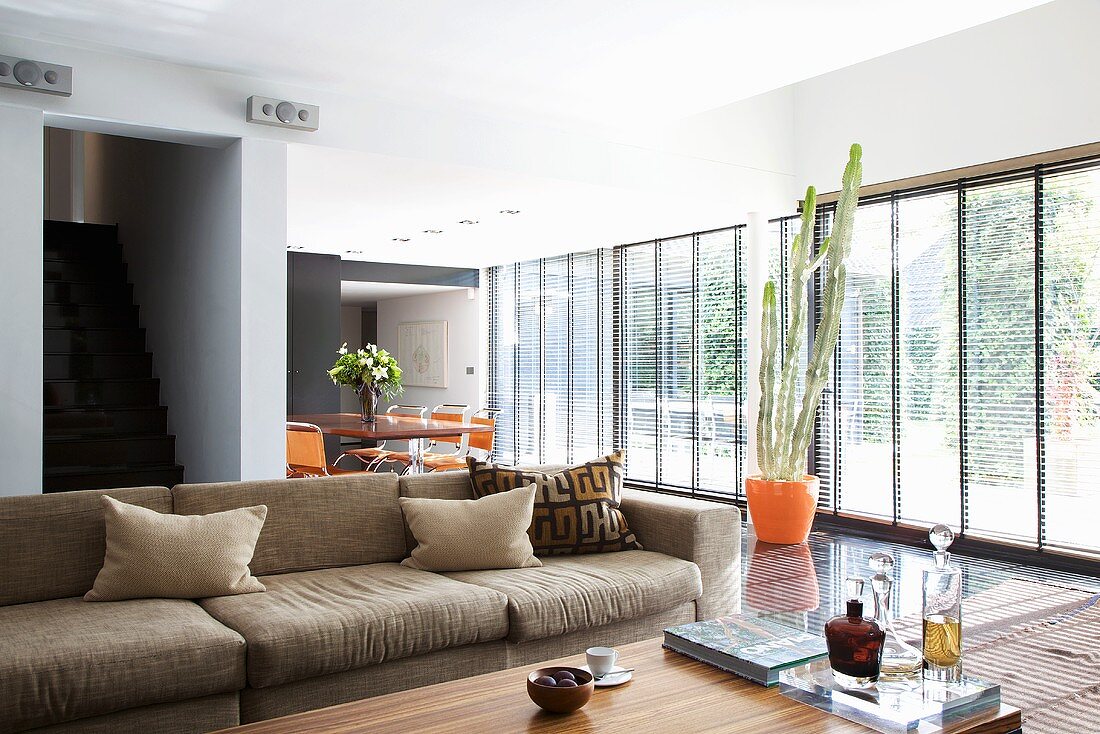 A spacious living room with a window bank and a brown sofa with cushions