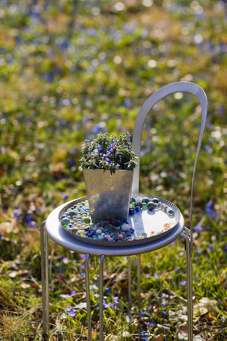 A flower pot on a tray of glass beads on a metal garden chair