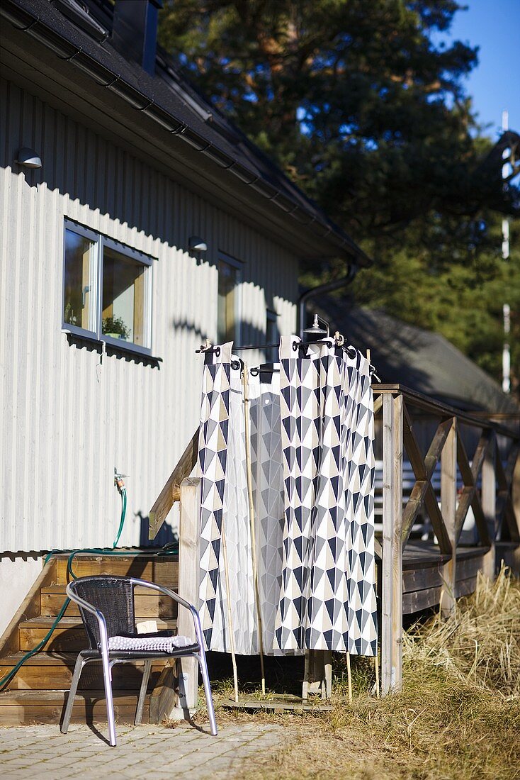 A weekend house - a chair in front of an outdoor shower with a curtain
