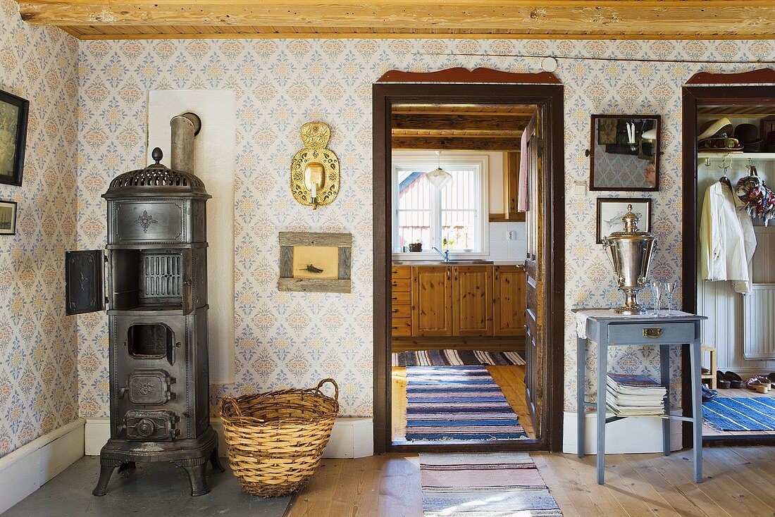 A living room in a country house - a fireplace against a papered wall and a view into the kitchen