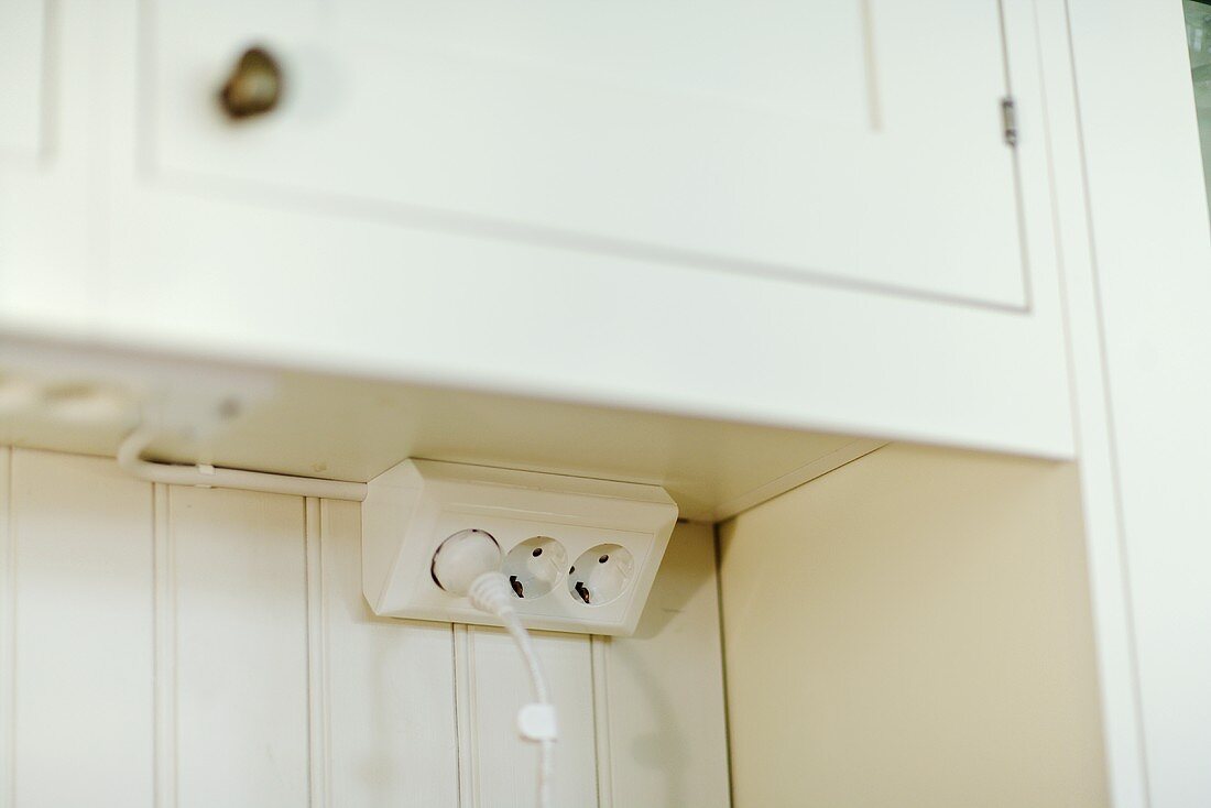 Electrical outlet under a kitchen cabinet with white doors
