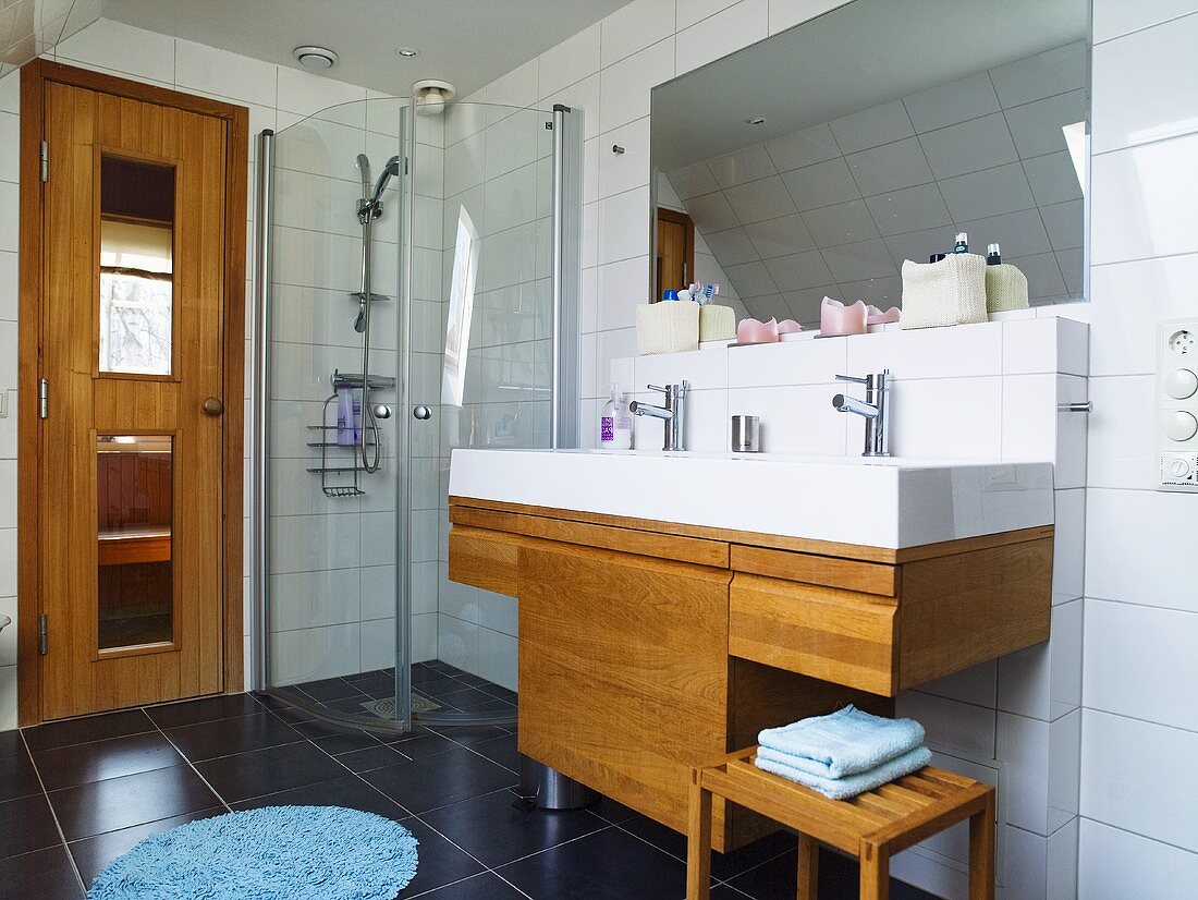 A tailored made washstand with a wooden cupboard underneath and a glass shower cubicle next to it