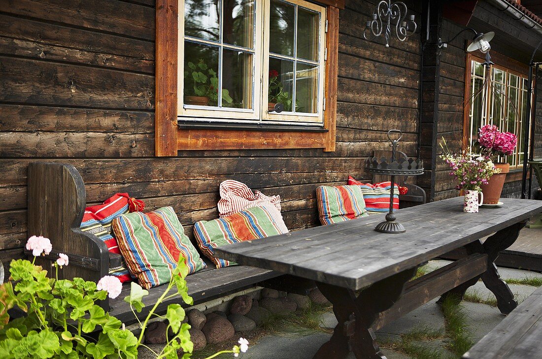 Rustic wooden patio table with colorful pillows in from of a wooden facade with windows
