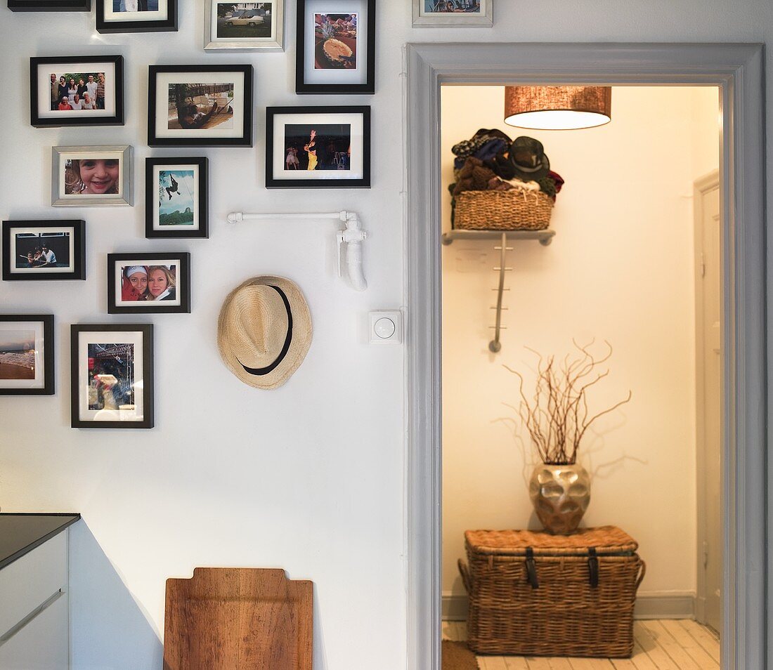 A collection of pictures hanging on the wall and a view into an illuminated hallway with a basket in front of the door