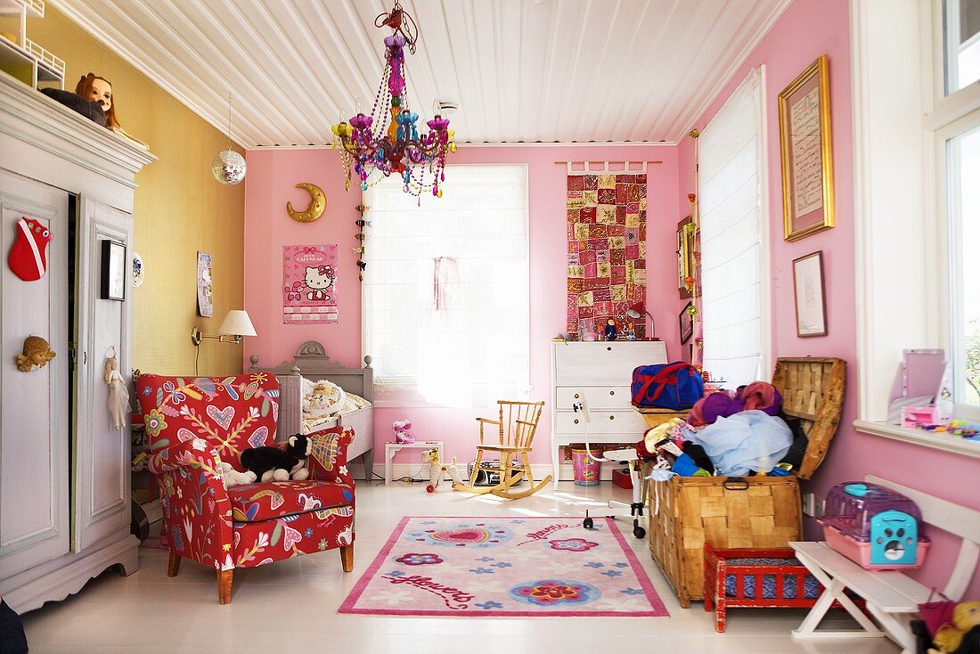 Kinderzimmer mit Lesesessel und Spielzeugtruhe vor farbigen Wänden und weisser Holzdecke