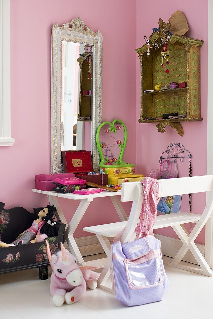 A corner of a child's room - a white bench and table in front of a mirror hanging on a pink wall