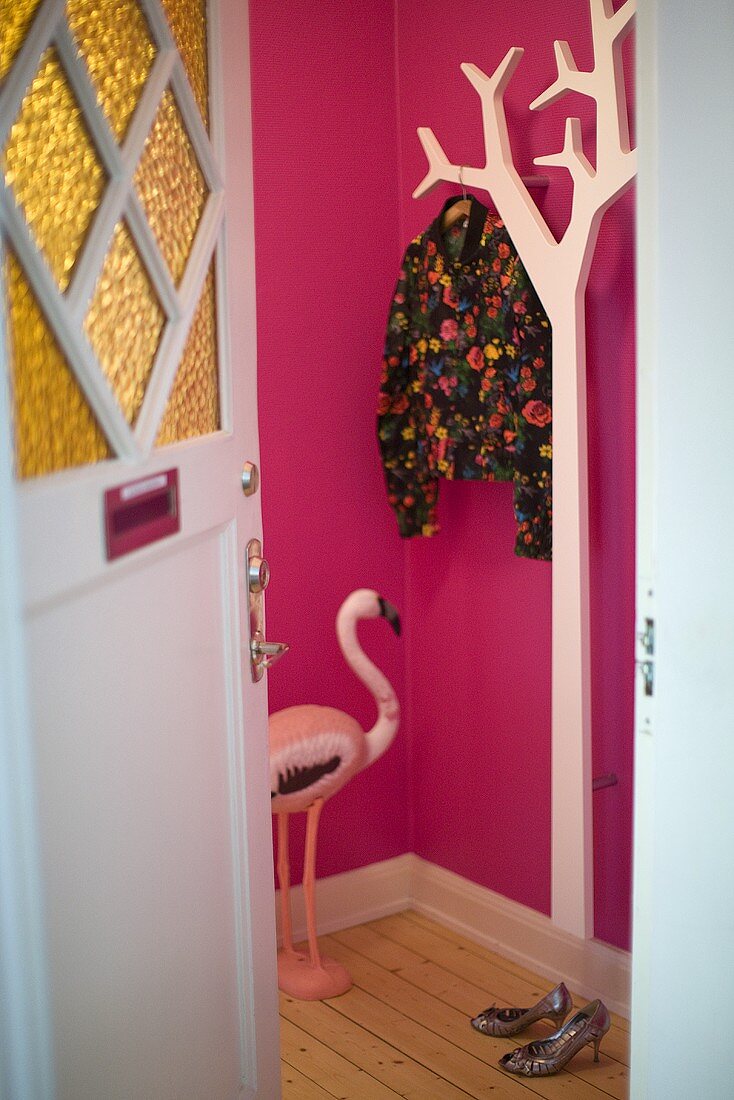 Offene Wohnungstür mit Blick auf weiße Garderobe an pinkfarbener Flurwand