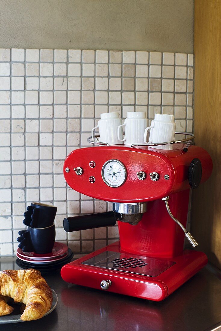 Rote Espressomaschine mit Kaffeetassen und Croissant in Küchenecke mit weissen Mosaikfliesen