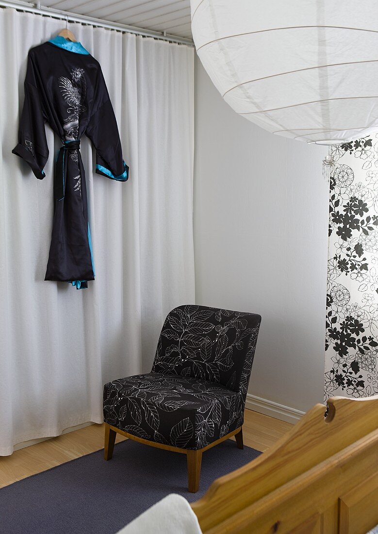 A corner of a bedroom - a chair in front of a curtain and a black kimono hanging up
