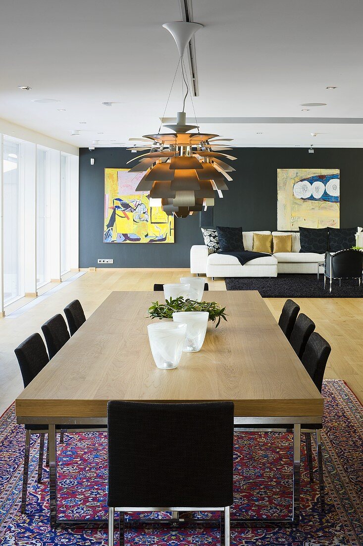 A dining table with a wooden top and designer lamp in an open-plan living-room-cum-dining-room with a view of a sofa