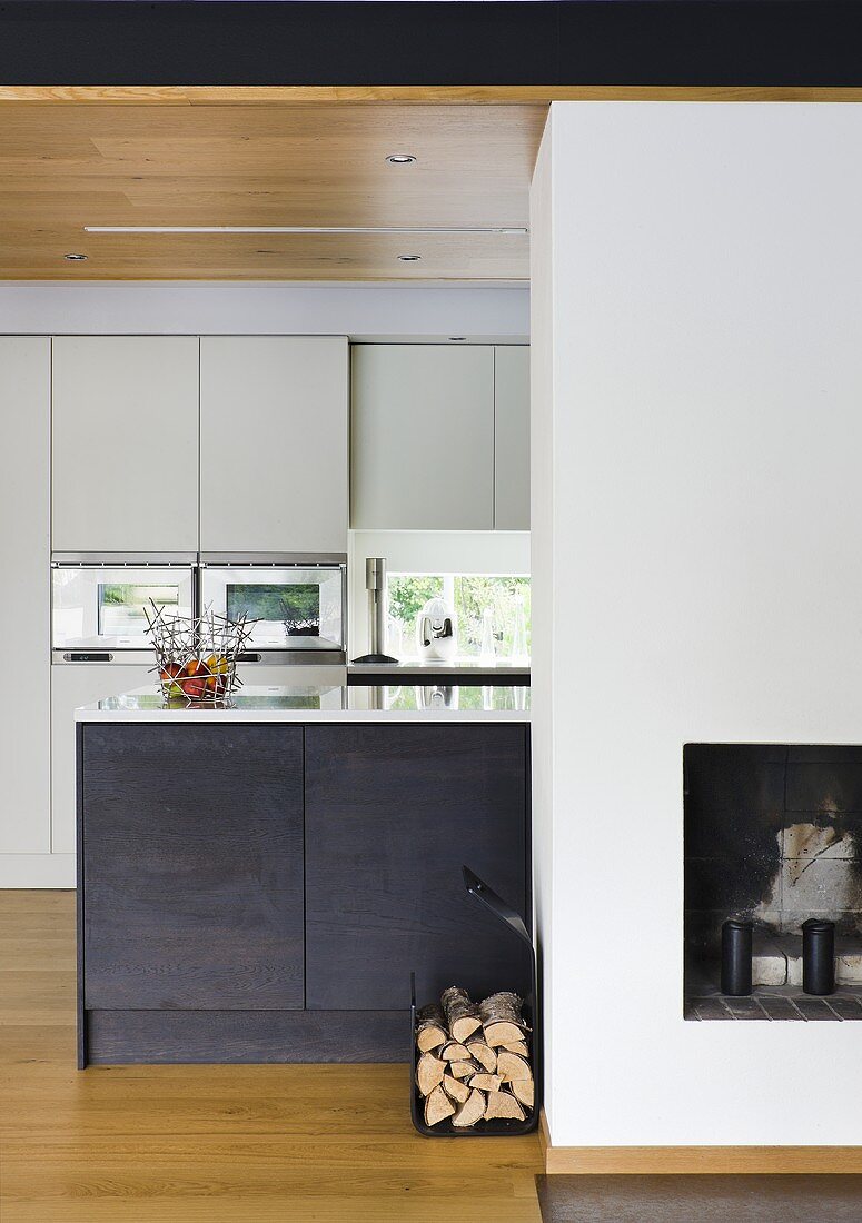 A kitchen counter with black cupboards in front of a white built-in cupboard and a fireplace