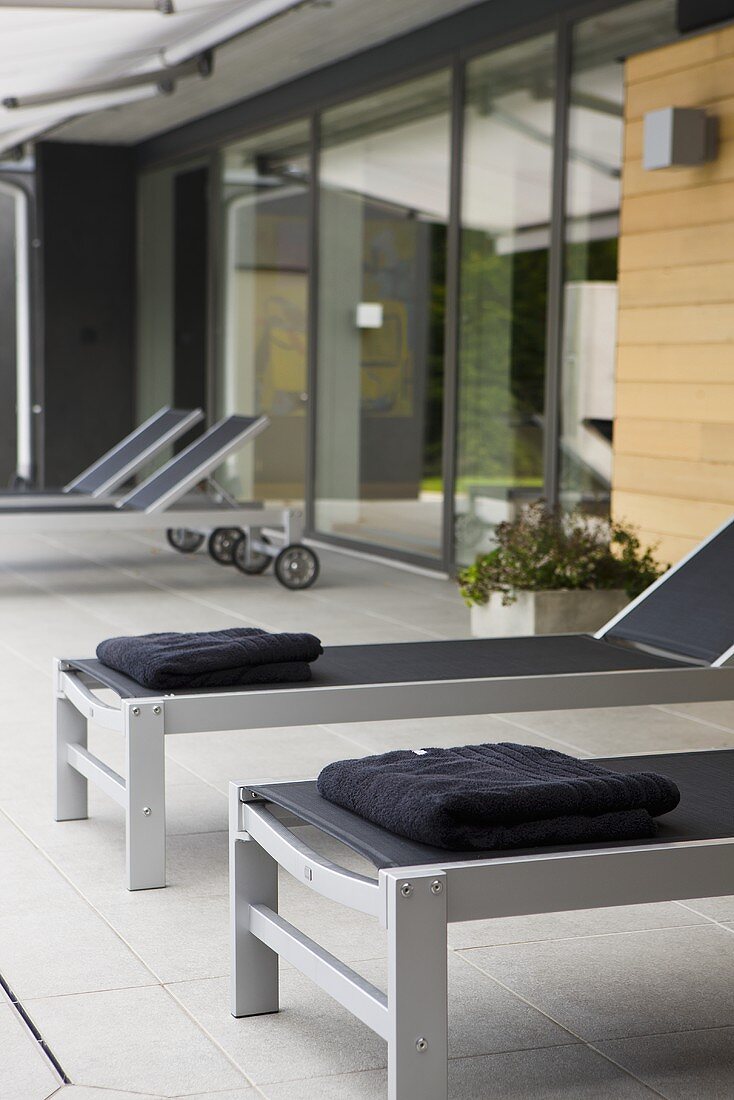 Designer Liegestühle auf graugefliester Terrasse vor dem Haus
