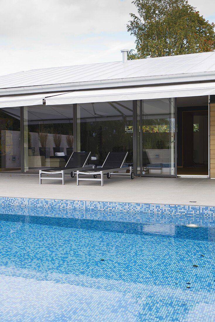 A poll with blue mosaic tiles in front of a house with a glass front and a covered terrace