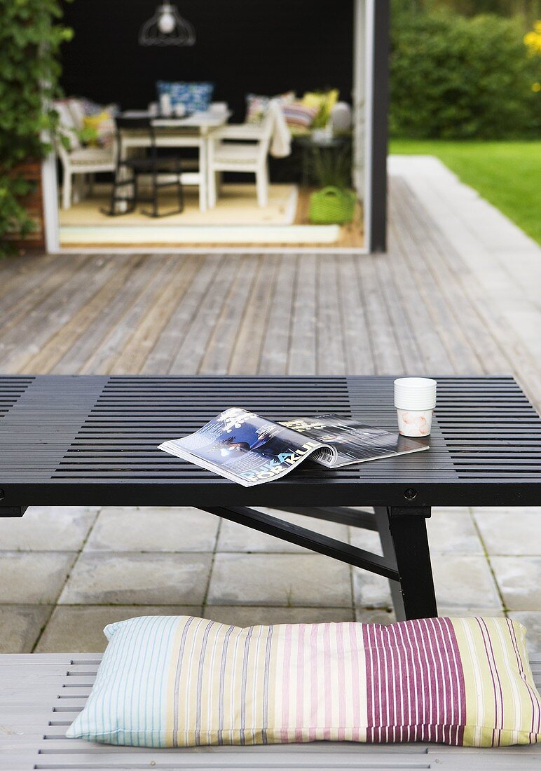 A black wooden table on a terrace with a view of a conservatory