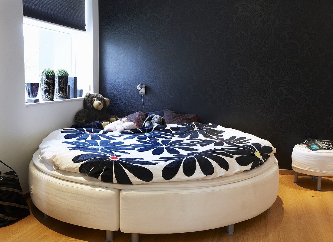 Schlafraumecke - rundes Bett mit Blumenmuster auf Bettwäsche vor schwarzer Wand