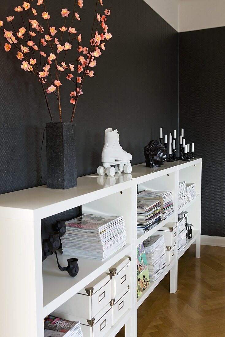 A corner of a room with black walls and a white half shelf with illuminated twigs in a vase