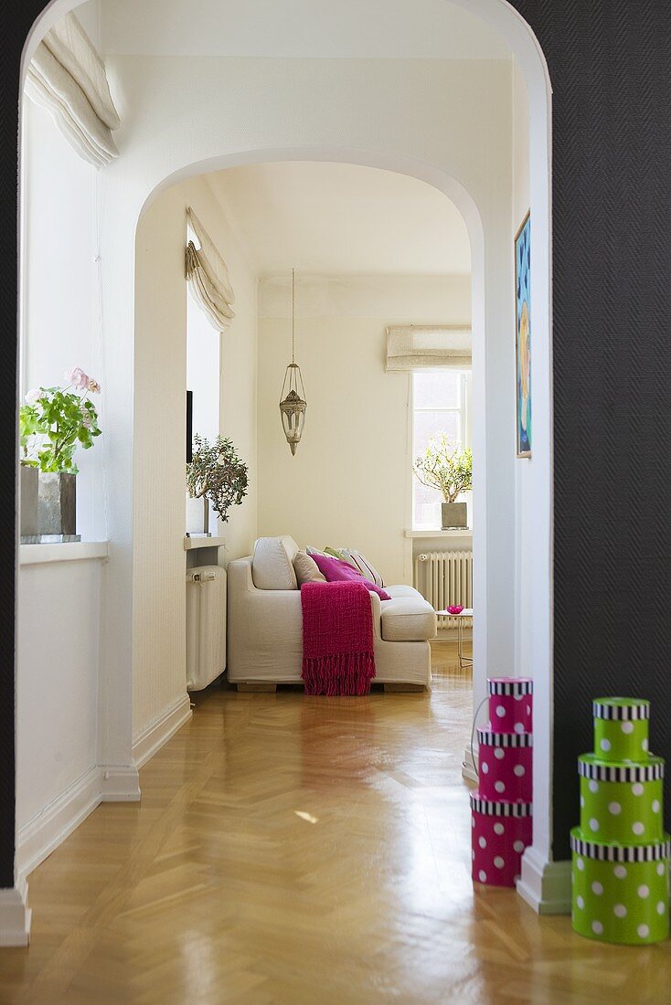 A view along a corridor with stacks of decorative boxes, through an archway into an Art Nouveau living room
