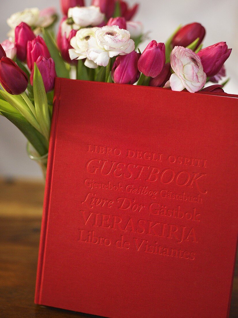 Blumenstrauss mit Tulpen und Rosen und Buch mit rotem Einband