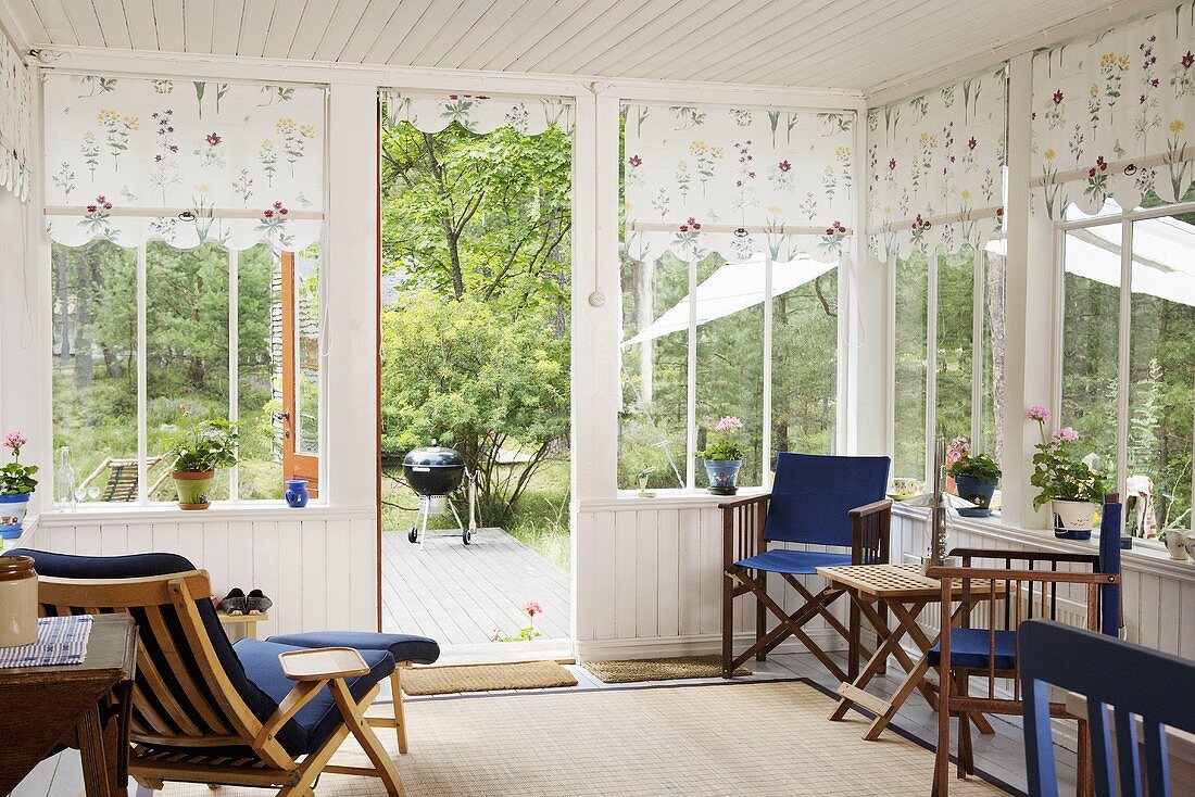 Wooden chairs in a conservatory with white wooden panelling and floral fabric blinds at the windows