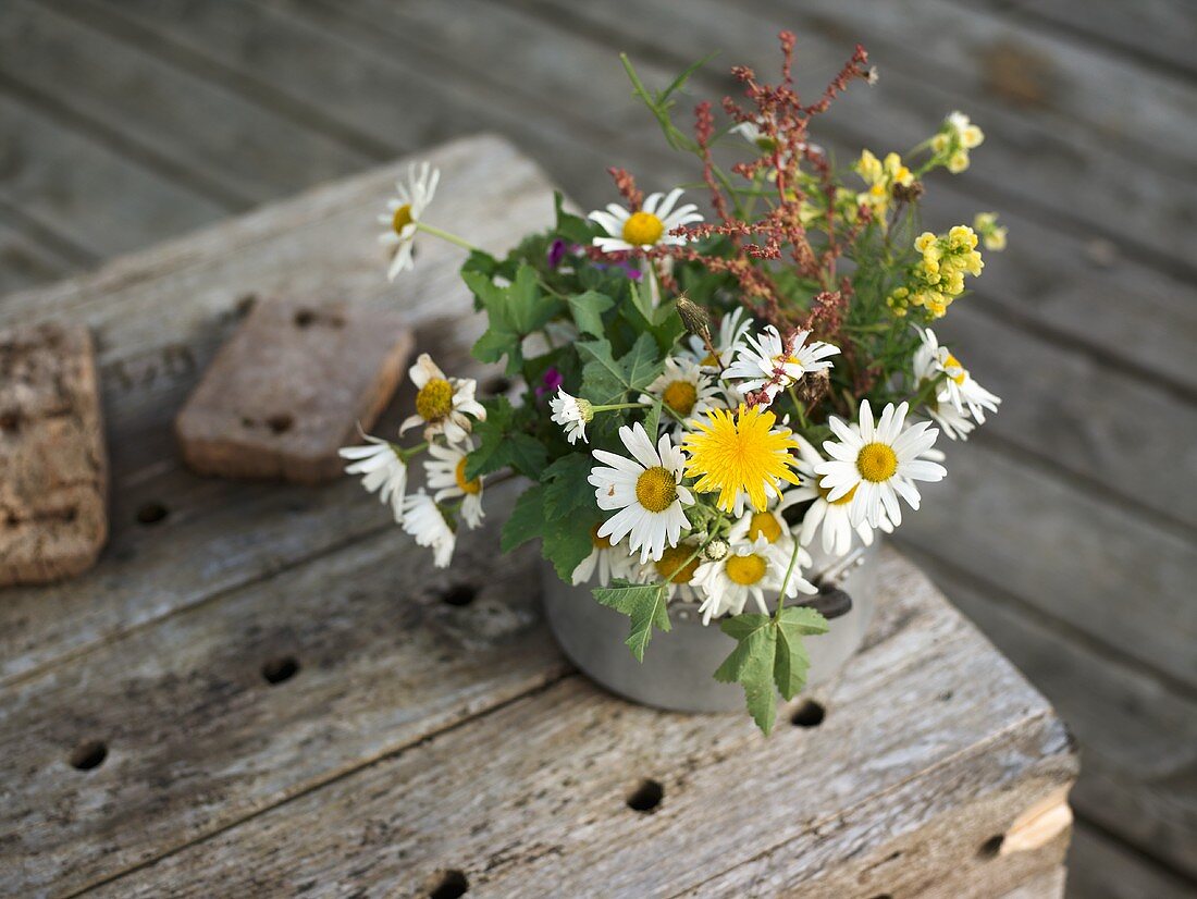 A bunch of meadow flowers in a metal pot on an old wooden shelf