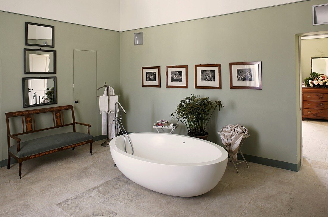 Freistehende Badewanne vor grauen Wänden auf Steinboden und antike Sitzbank