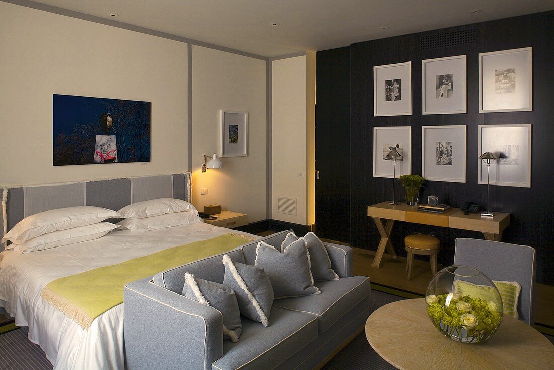 Doppelbett und graue Sofagarnitur im Schlafraum mit Schreibtisch und Bildersammlung vor schwarzer Wand