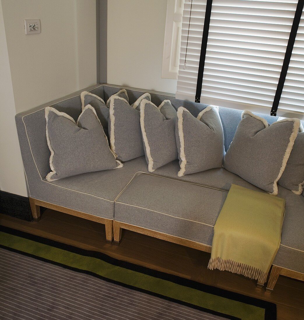Light gray sofa and pillows covered in the same material in a bay window in front of closed blinds