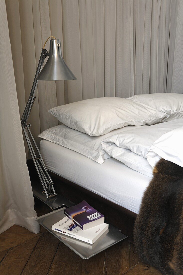 Stainless steel floor lamp next to a bed with gray curtains at the head