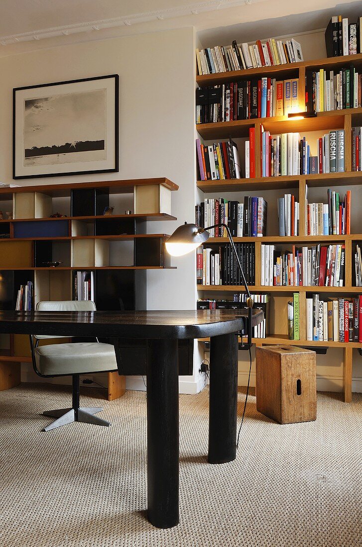 Black table in front of a illuminated book shelves in a wall niche and wall shelving in 50's style