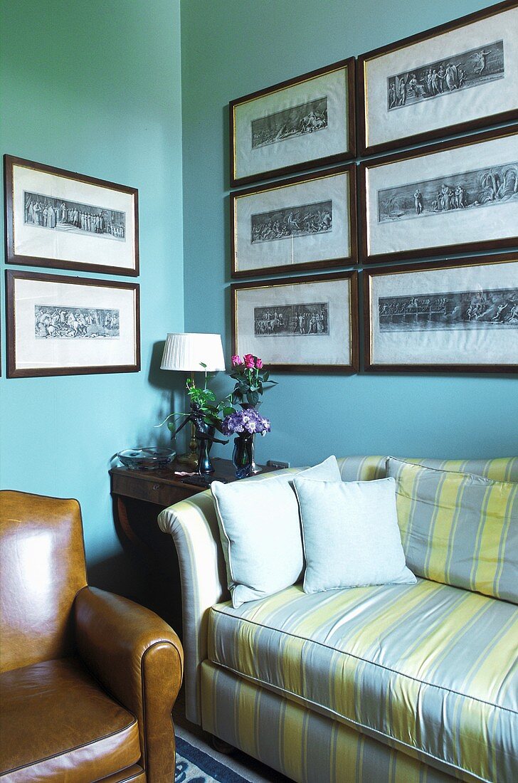 Corner of a living room painted turquoise with a sofa and a collection of pictures on the wall