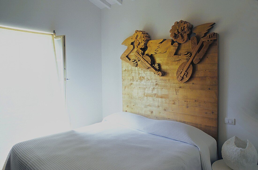 Weisser Schlafraum mit Doppelbett und Kopfteil aus Holzplatte mit Engelsfiguren