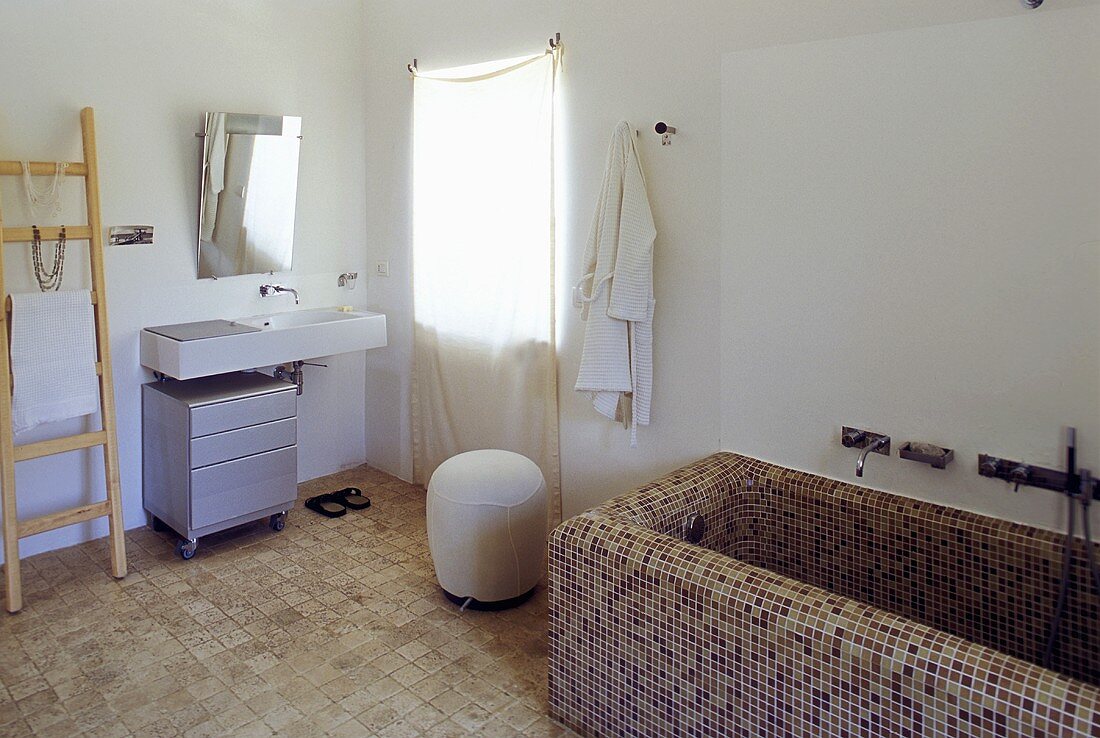 Country style bathroom -- bathtub with brown mosaic tiles and washstand with a mirror by the window