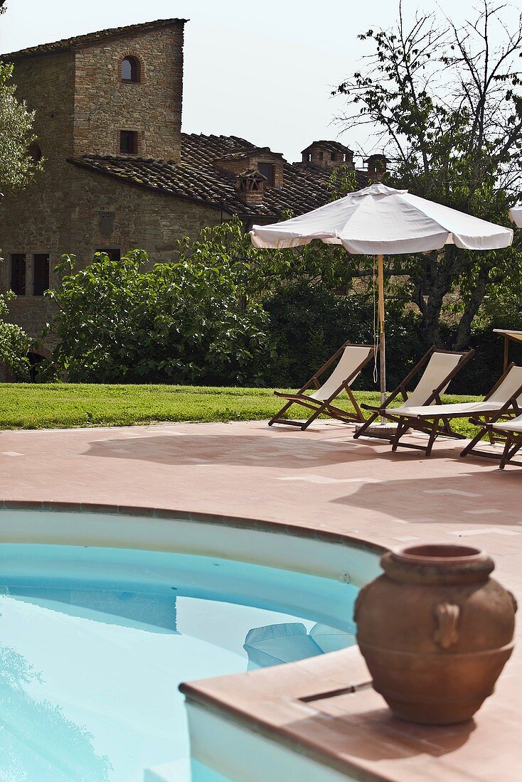 Tongefäss am Pool und Liegestühle unter Sonnenschirm mit Blick auf Mediterraner Gehöft