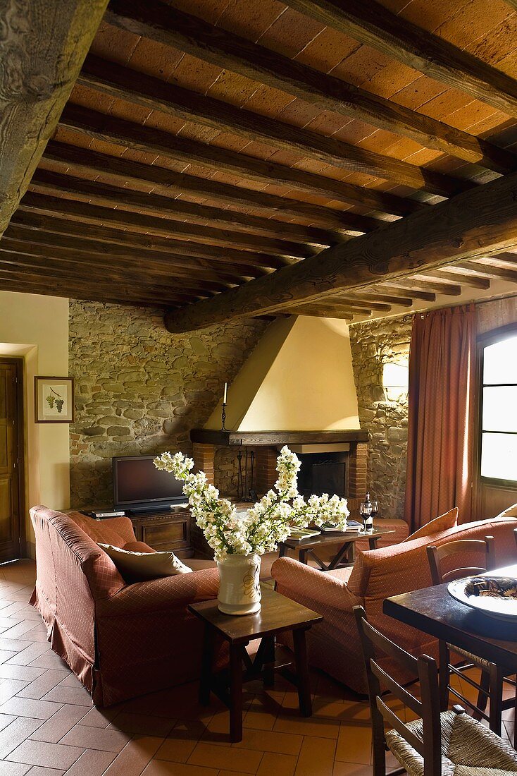 Living room with a rustic wooden ceiling and living room suite in front of an inglenook made of natural stone