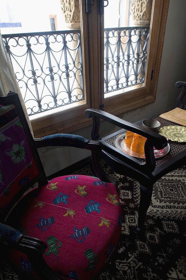 Gepolsterter Stuhl und schwarzer Beistelltisch vor Fenster mit Brüstungsgitter