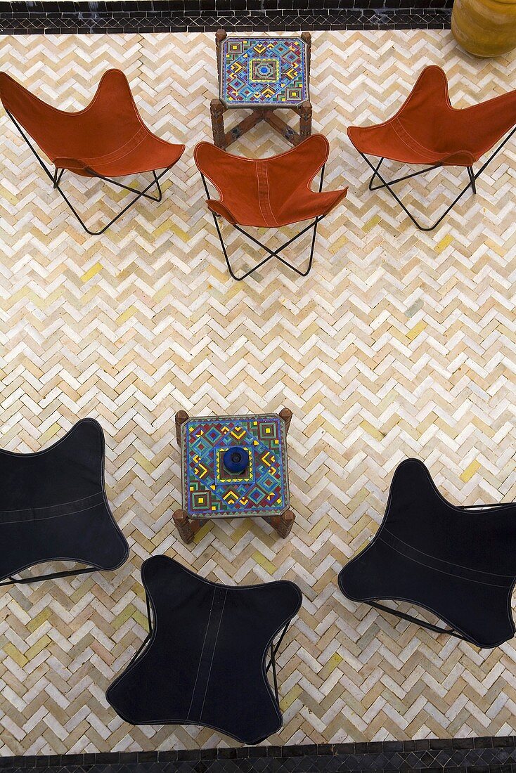 Blick auf Klassikerstühle in braunem und schwarzem Bezug mit orientalischen Beistelltischen und Fliesenboden im Fischgrätmuster