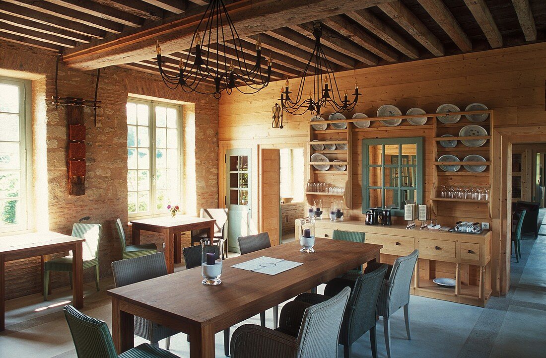 Grosszügiger Essraum mit einer Holzbalkendecke in einem Landhaus, langer Esstisch mit Korbstühlen