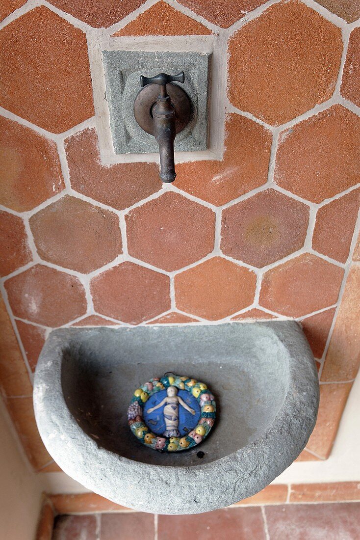Stone sink and old faucet in front of a wall with terracotta tiles