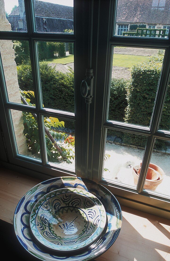 Auf der Fensterbank stehen gestapelte Schüssel, dahinter mit Aussicht auf den Garten